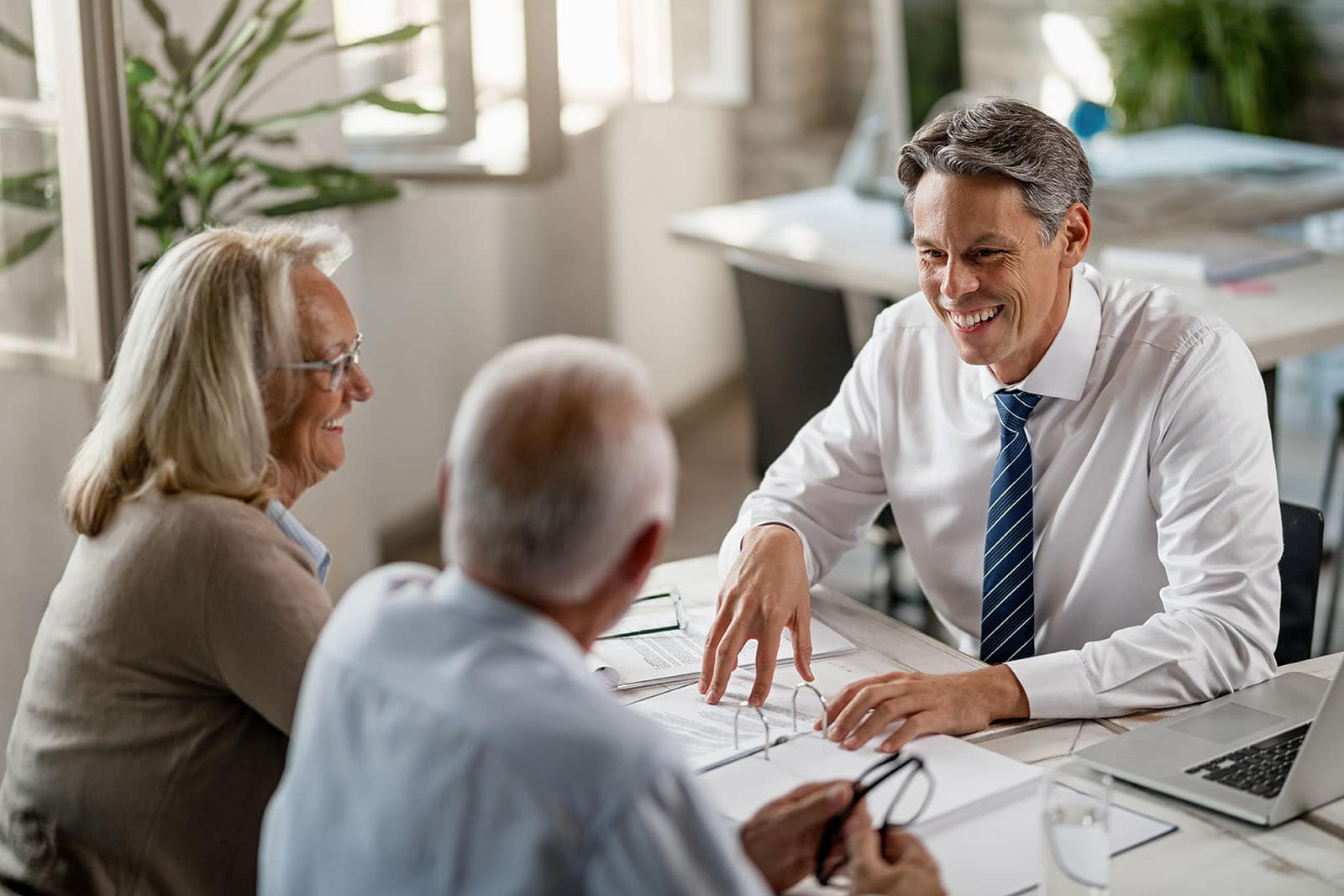 Happy insurance agent and senior couple talking while going through paperwork on a meeting in the office.